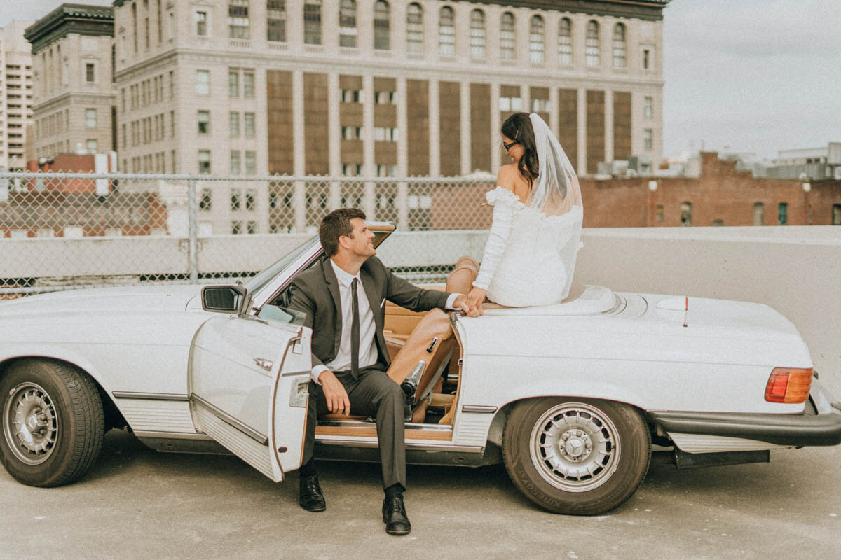 couple posing on a convertible on a rooftop parking garage