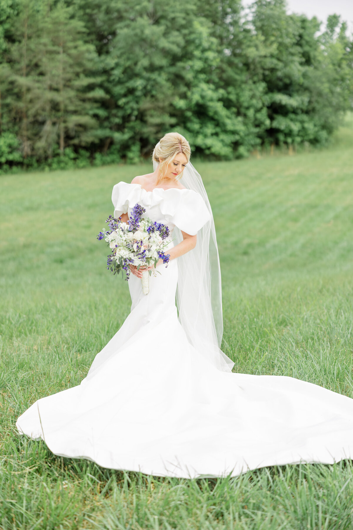 Bride looking down her shoulder at her glamorous dress in the meadow of Mossy Creek