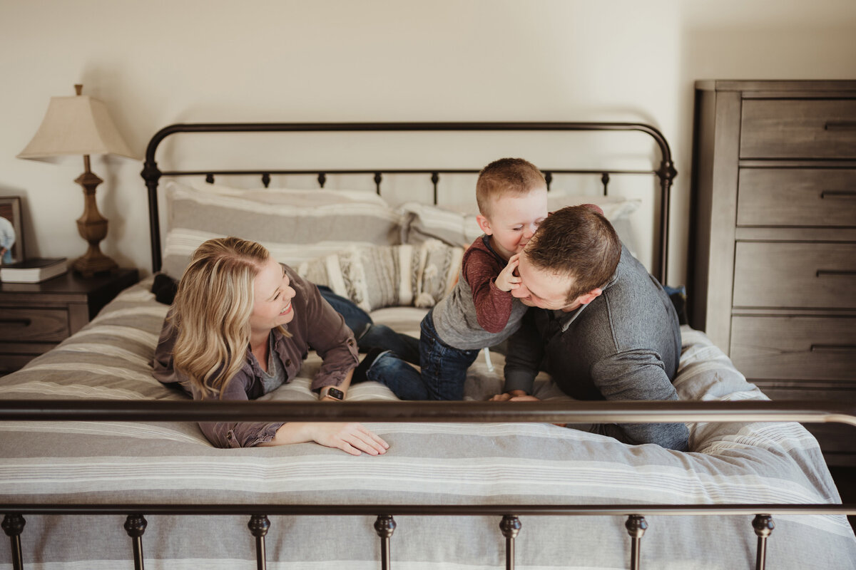 A family of three is lying on the bed playing.