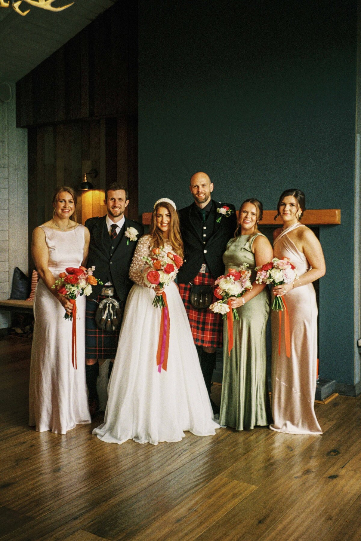 A bride and groom stand with their wedding party and smile for photography.  It is a 35mm film photograph.