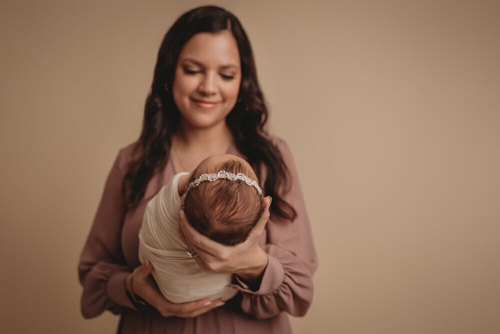 Mom and baby posing together for newborn session at Atlanta, Georgia newborn photographer studio. Mom is looking at baby smiling.