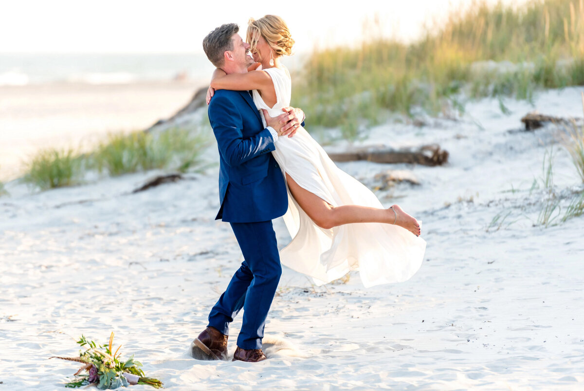 Groom wearing a blue suit, twirling his bride on the beach in Brigantine New Jersey