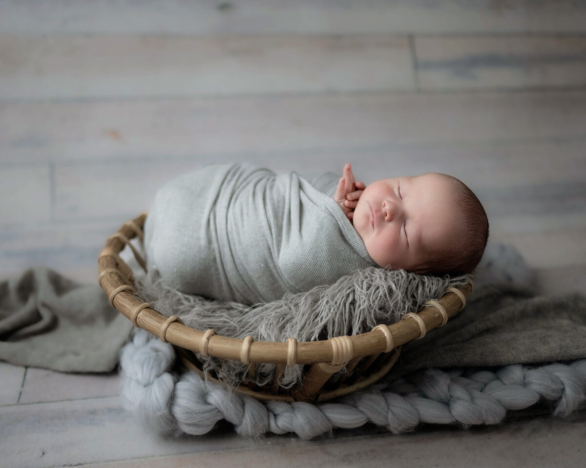 A newborn sleeping in a wicker basket on the floor of a studio under a window