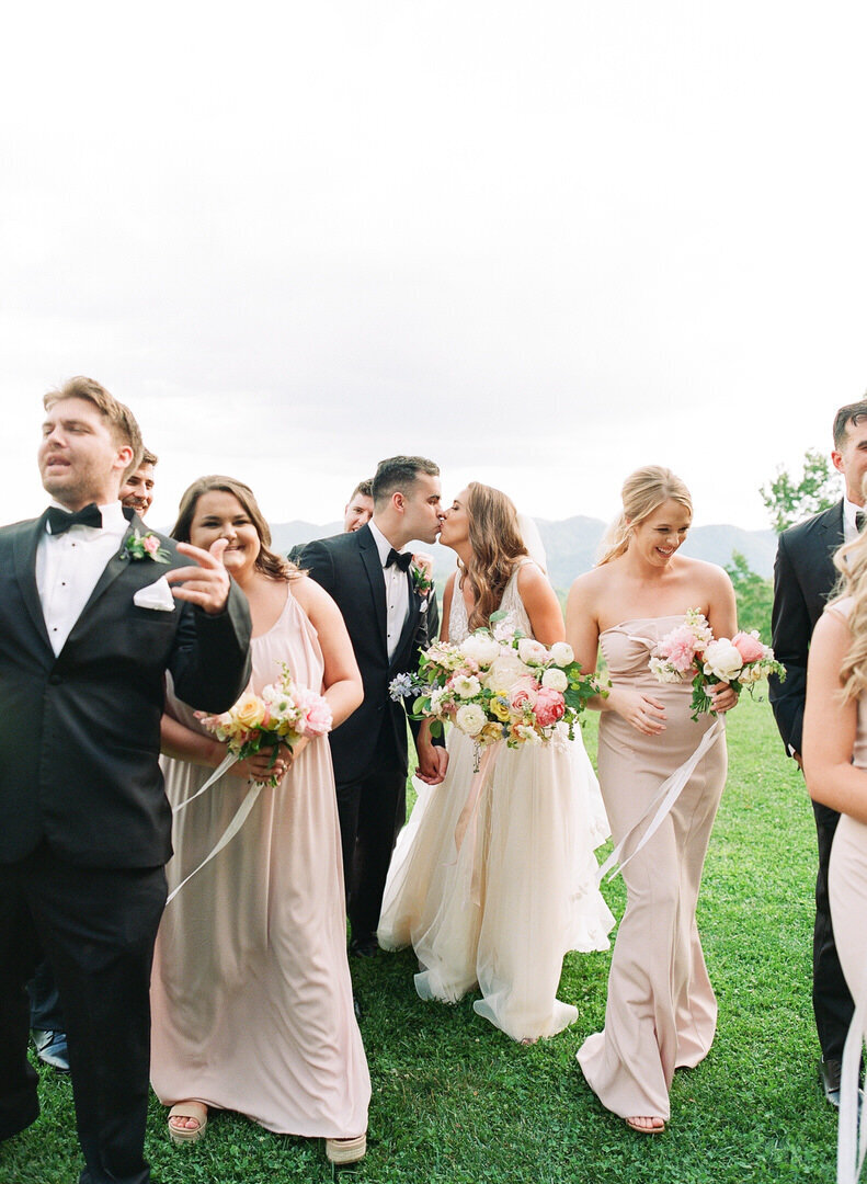 Bride and Groom Kissing Walking With Bridal Party Photo