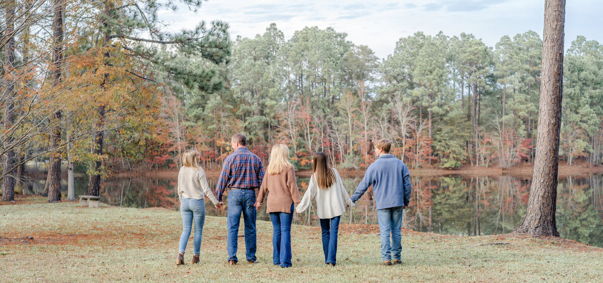 family of five walking hand in hand towards the small pond in the family's backyard