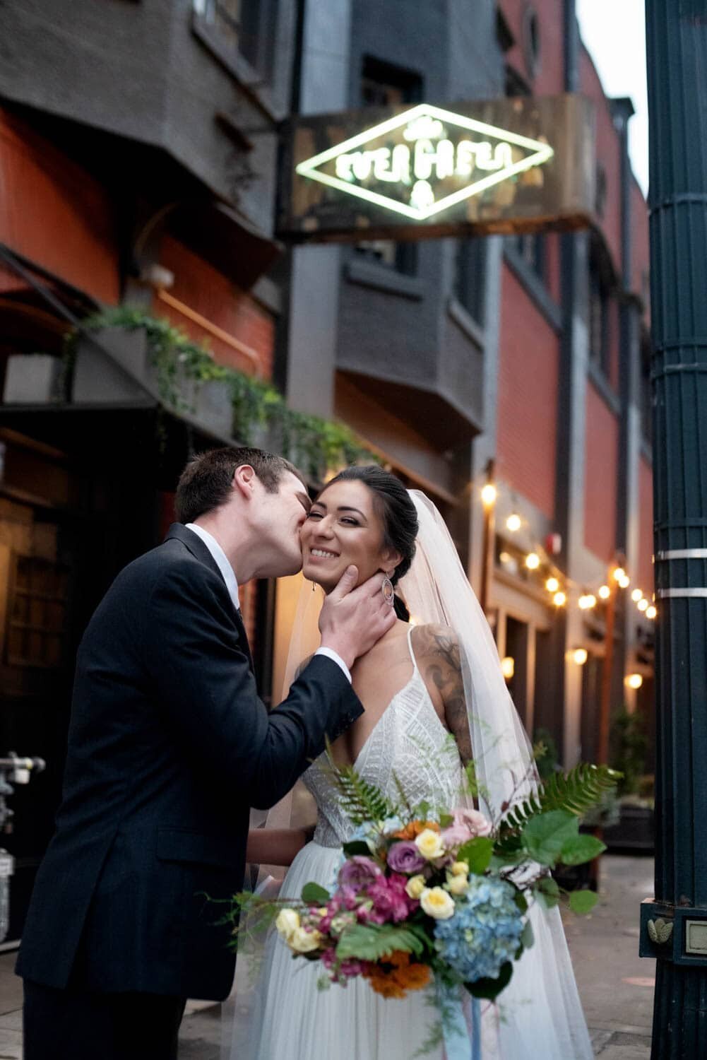 a man kisses a bride's cheek in front of The Evergreen in SE portland