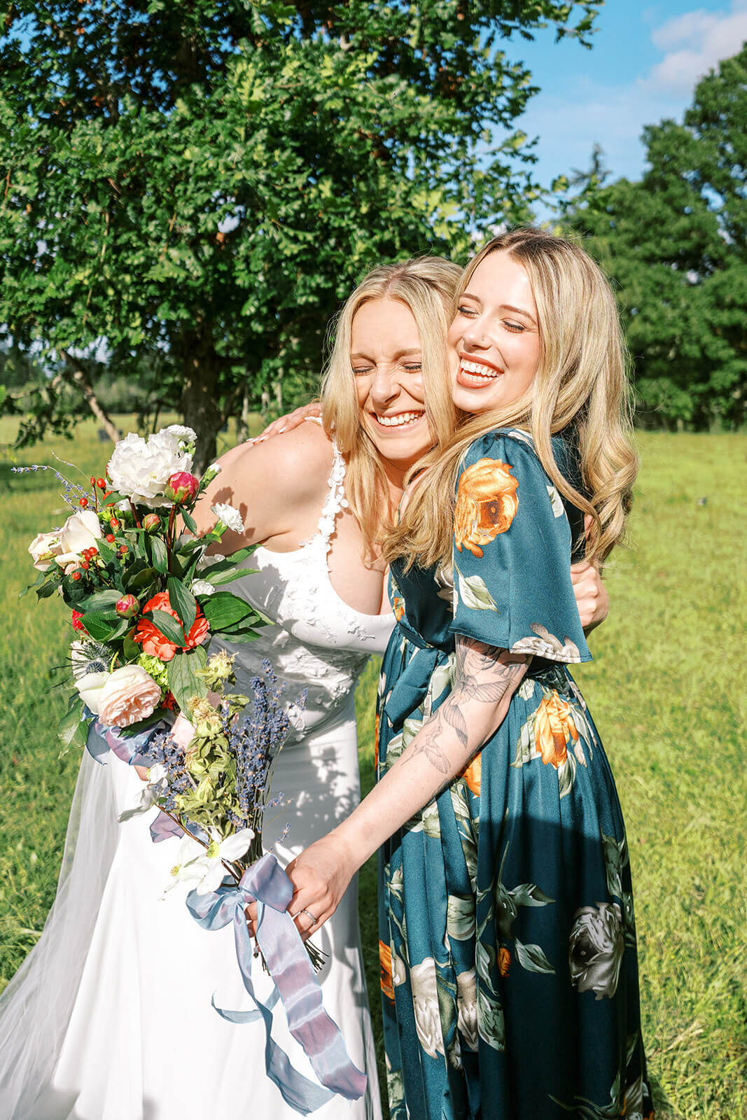 A bride hugs another woman and smiles at her outdoor Oregon wedding.