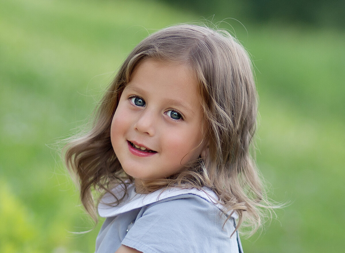 Little boy is sitting in a brooklyn park at a photoshoot  to commemorate his upsherin. He is looking over his shoulder and smiling at the camera. Captured by Chaya Bornstein, Brooklyn Family Photographer
