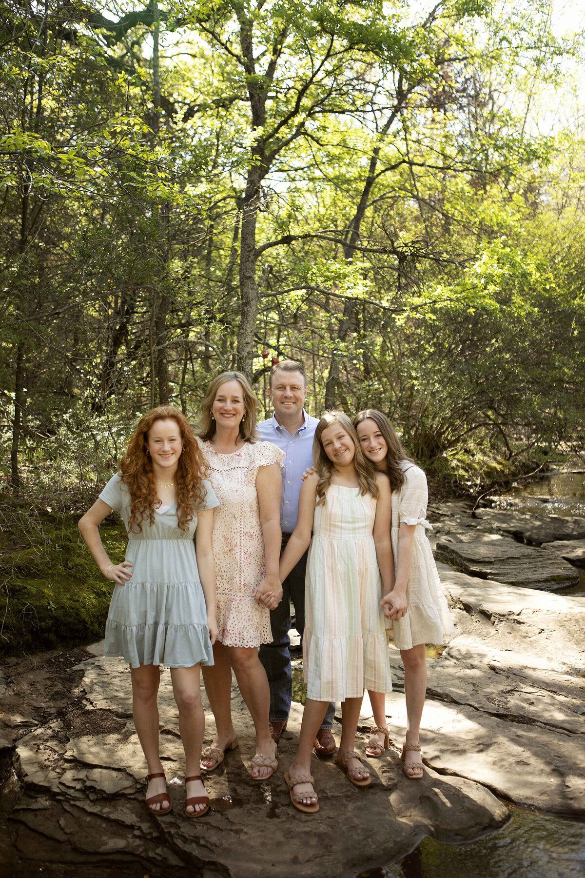 Family with three girls smiling and posing together by the creek, capturing a joyful moment in nature