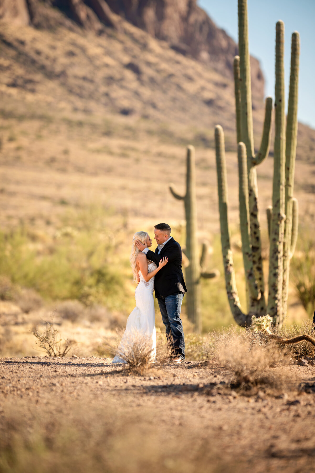 Bride and groom standing next to tall Saguaro cactus near superstition mountains