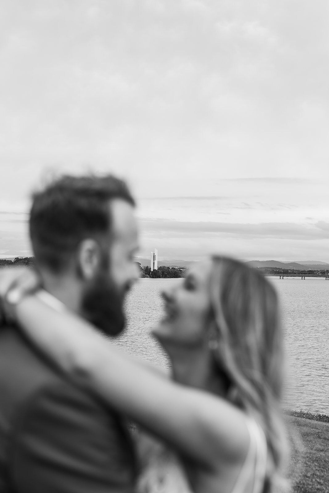 Bride and groom shown in foreground out of focus. The National Carillion and Lake Burley Griffin is in focus in the background 