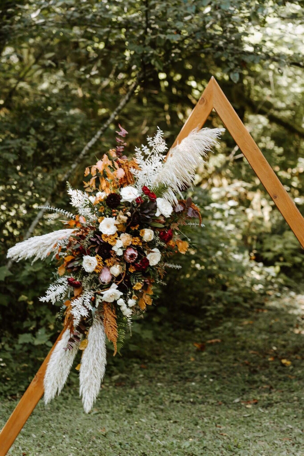 Floral installation on triangular  arbor features pampas grass and florals in fall colors.