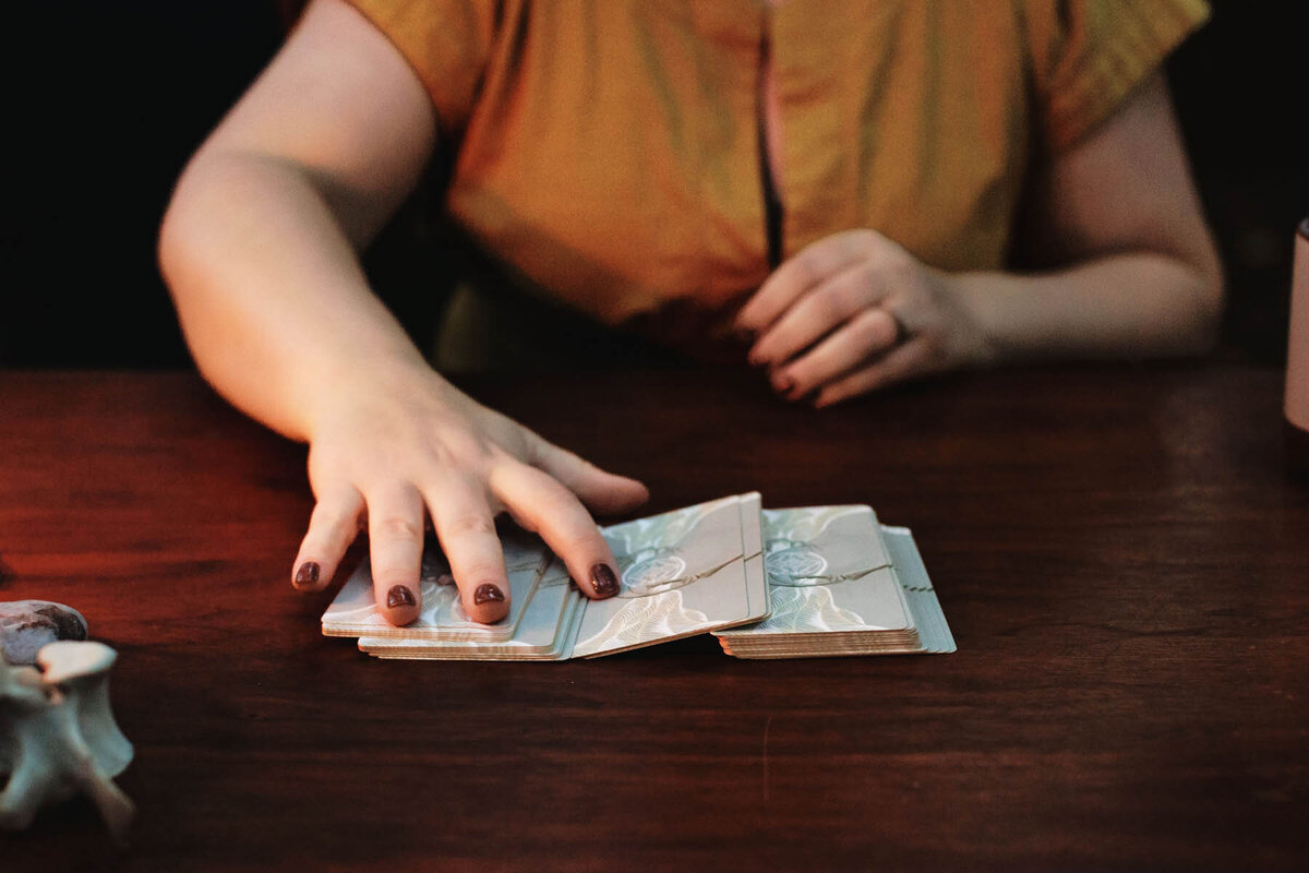 Energy worker Ash Stinson sits at a table and spreads out the cards of the Energy Archaeology Oracle Deck for a reading