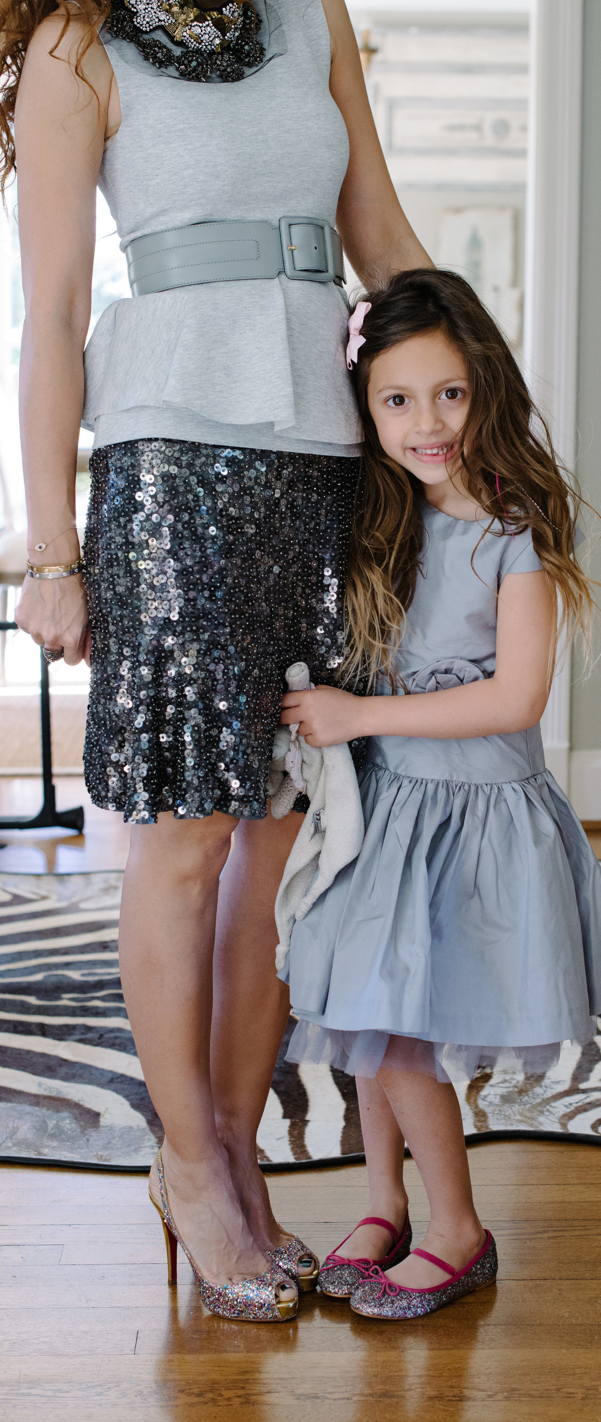 little girl in grey dress holding moms leg with glitter shoes