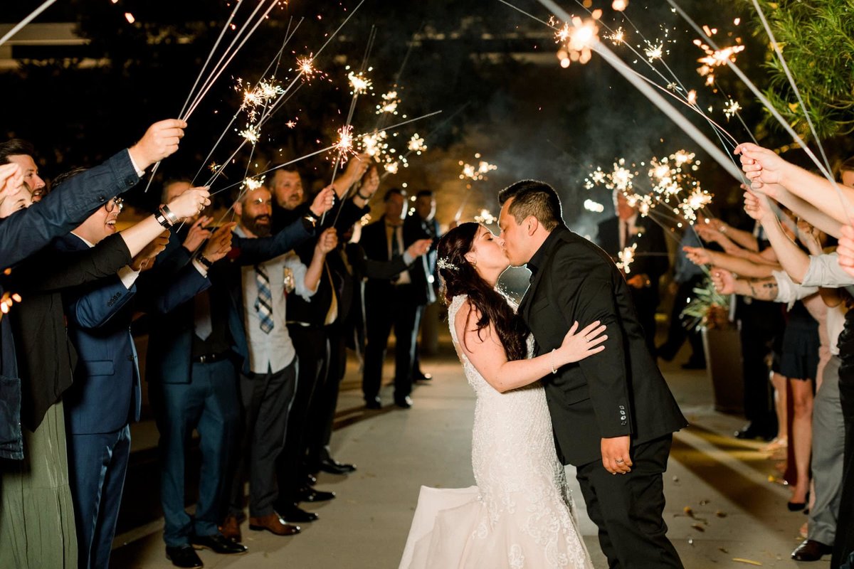 Bride and Groom stop for a kiss after walking under a tunnel of sparklers held by wedding guests