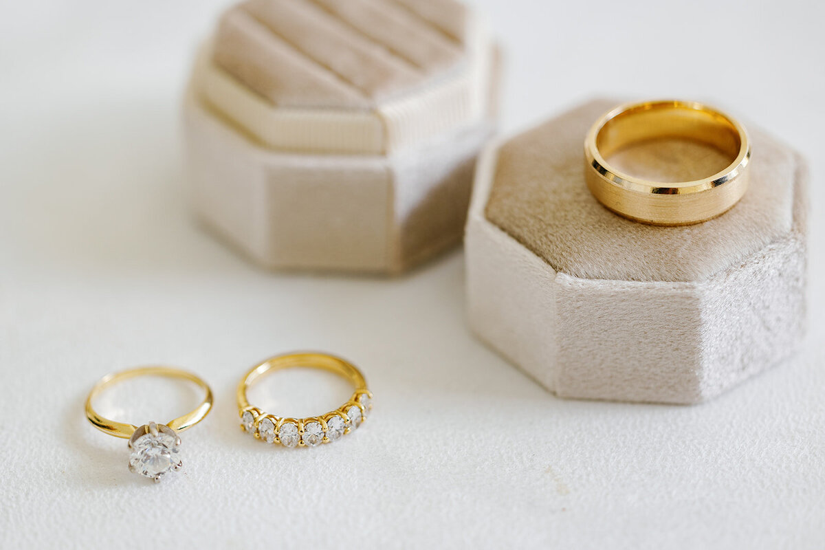 A soft, elegant detail shot featuring the couple’s wedding bands and solitaire engagement ring in neutral velvet ring boxes. Captured during Stephanie and Bradley’s wedding by Claudia Amalia Photography.