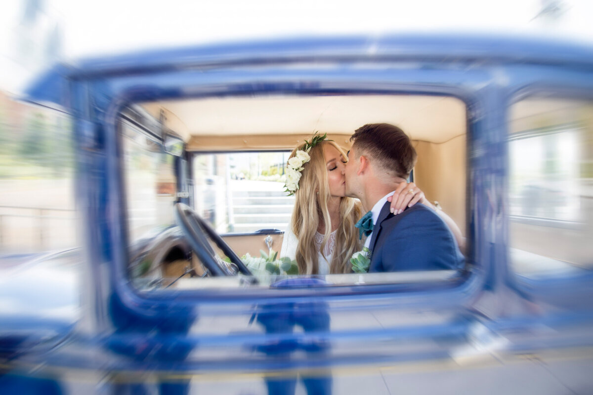 Stunning wedding photography of a bride and groom kissing in a blue vintage car