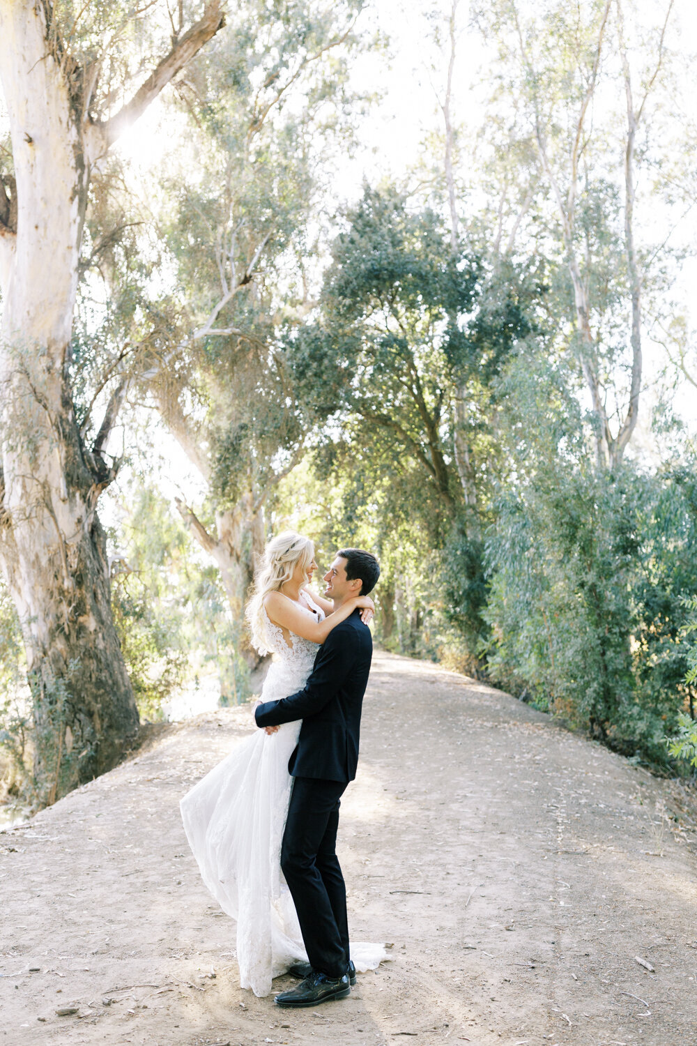 groom picking up his bride on a dirt road under the eucalyptus trees