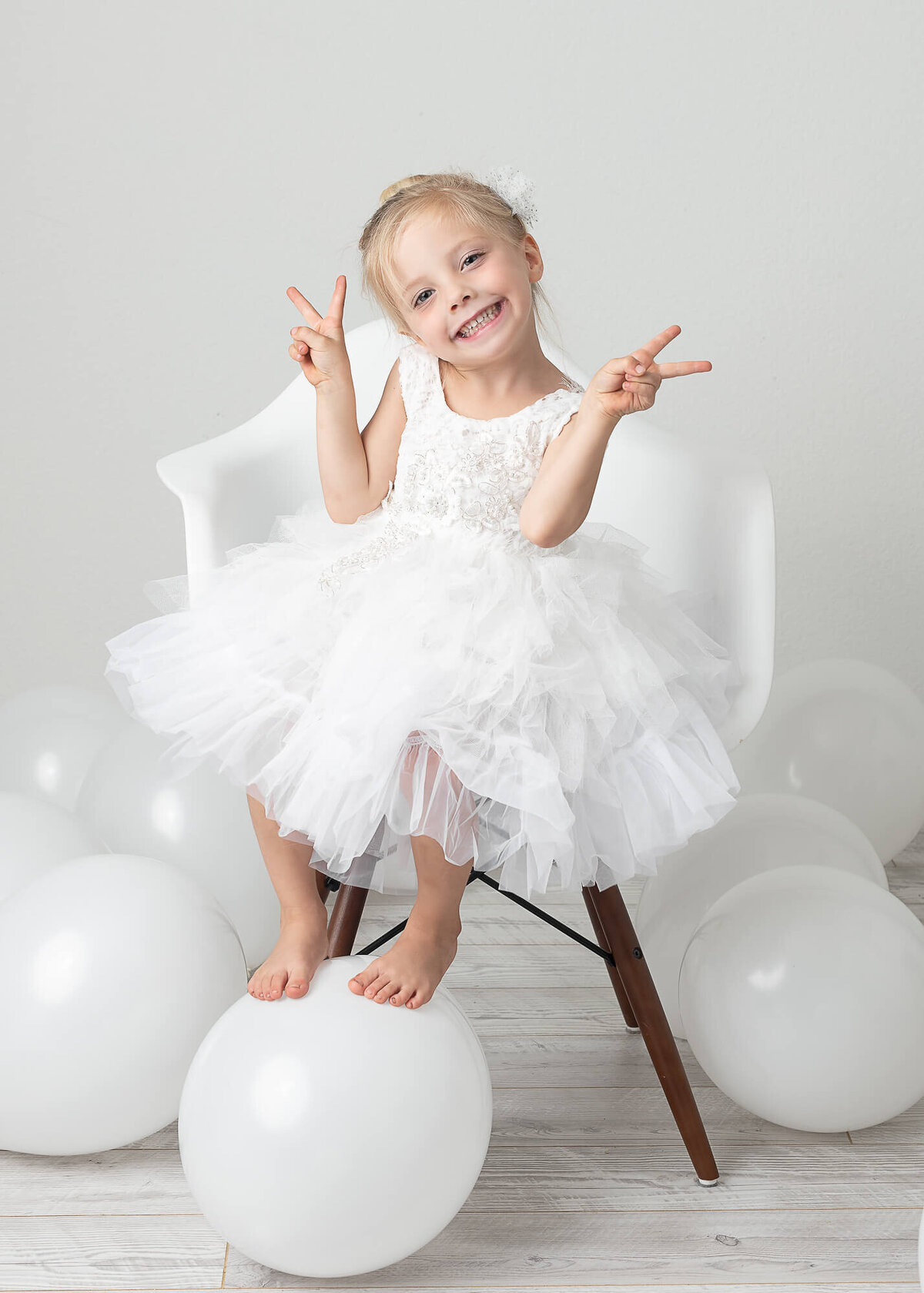 girl in tutu sitting on eames chair with balloons surrounding her