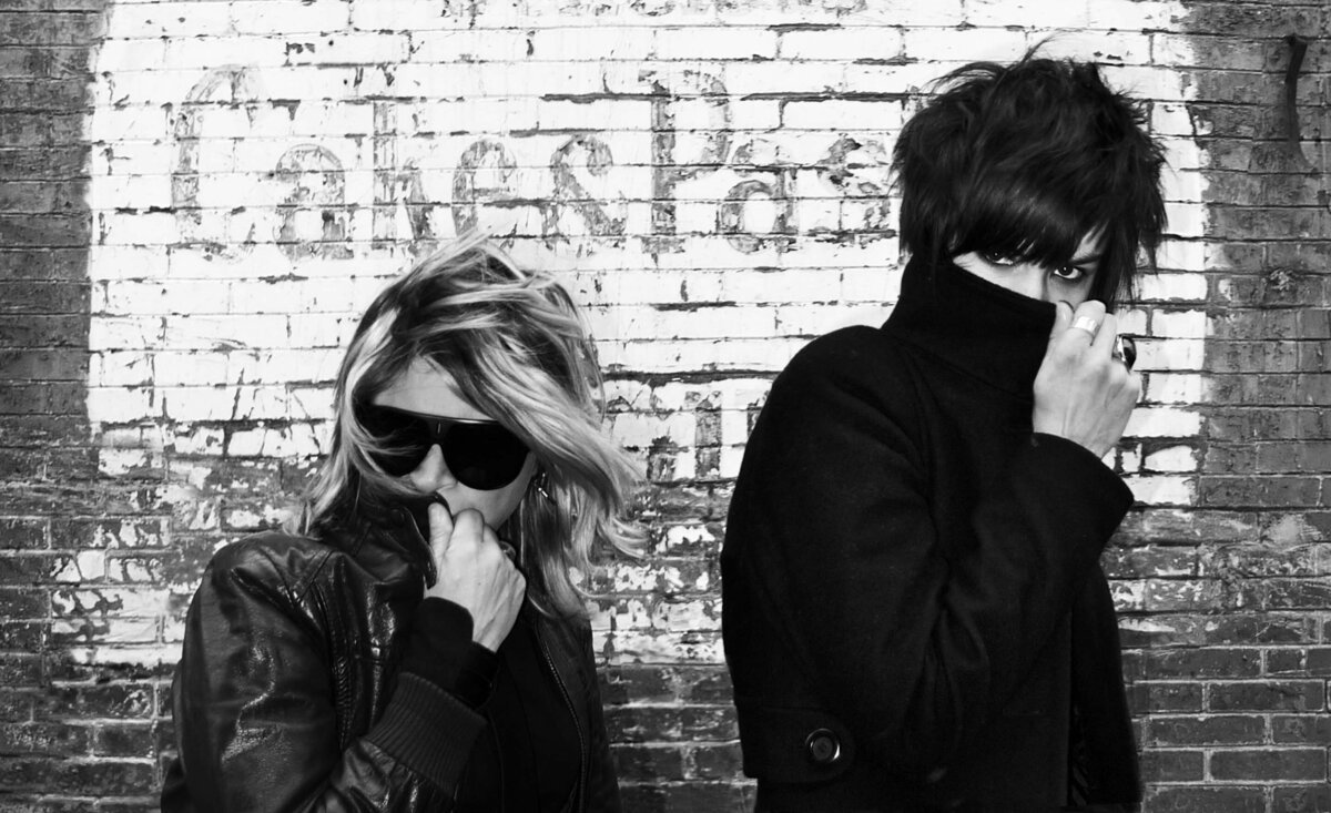 Musical duo portrait The Pack A.D. black and white hiding faces with coat collars against old painted brick wall