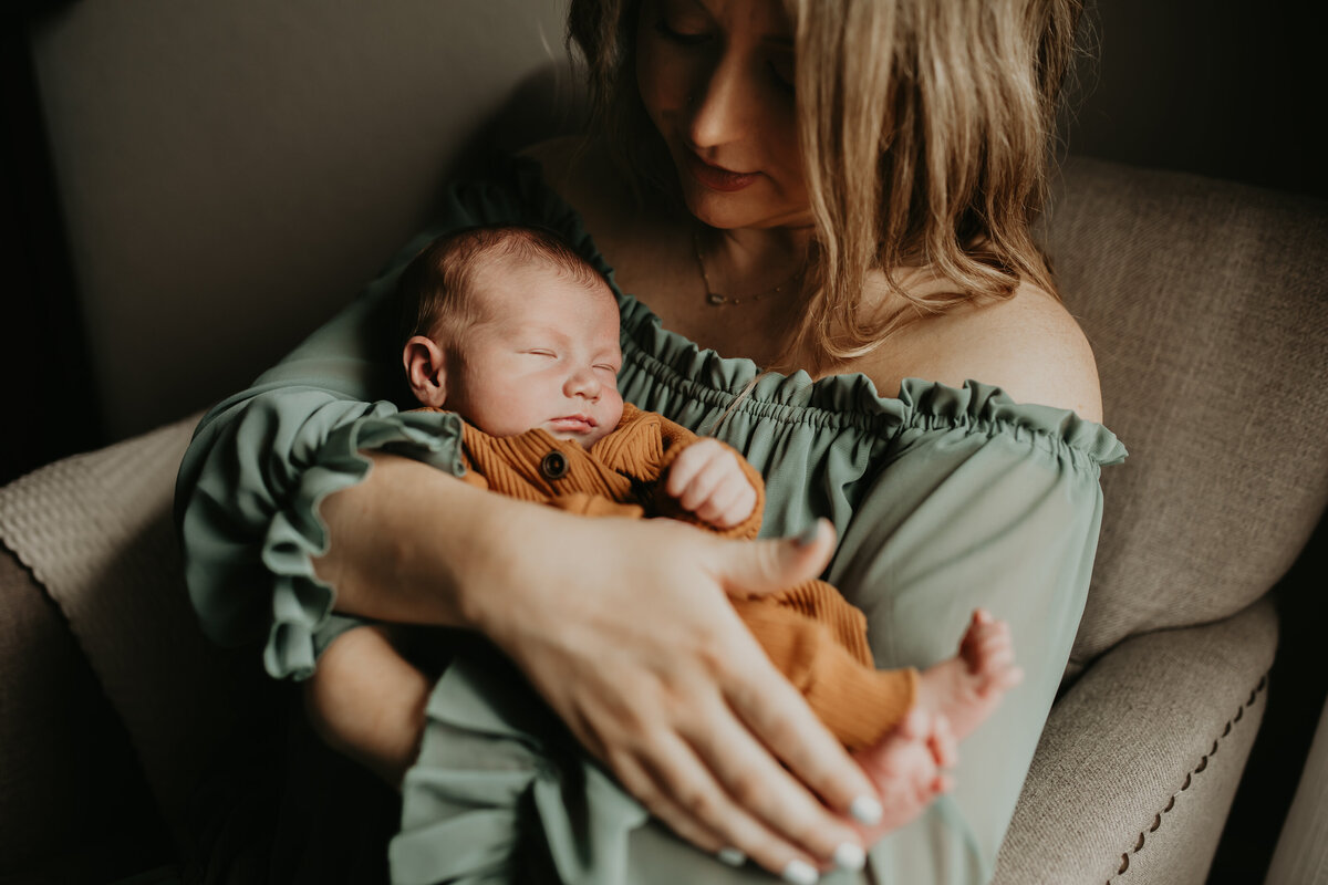 Mother holds newborn baby during in-home newborn session with premiere newborn photographer, Cameron Fox of Foxc Photography, in Burleson, Texas.