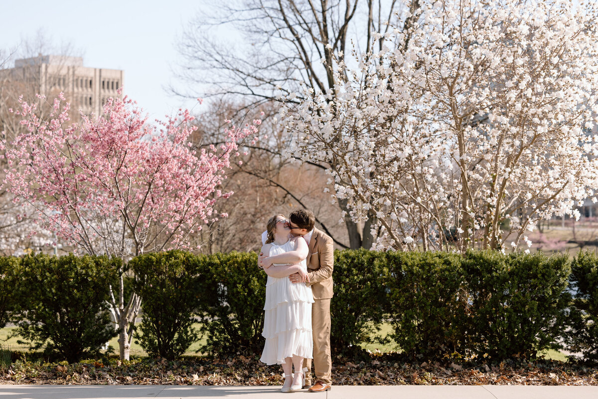Bride and groom kissing in front of blossoming trees at Wade Lagoon.