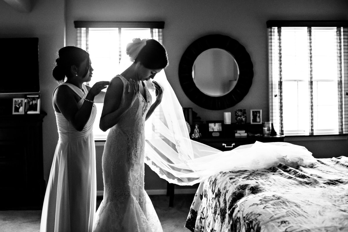 The maid of honor helps a bride put on her wedding dress in her childhood bedroom.