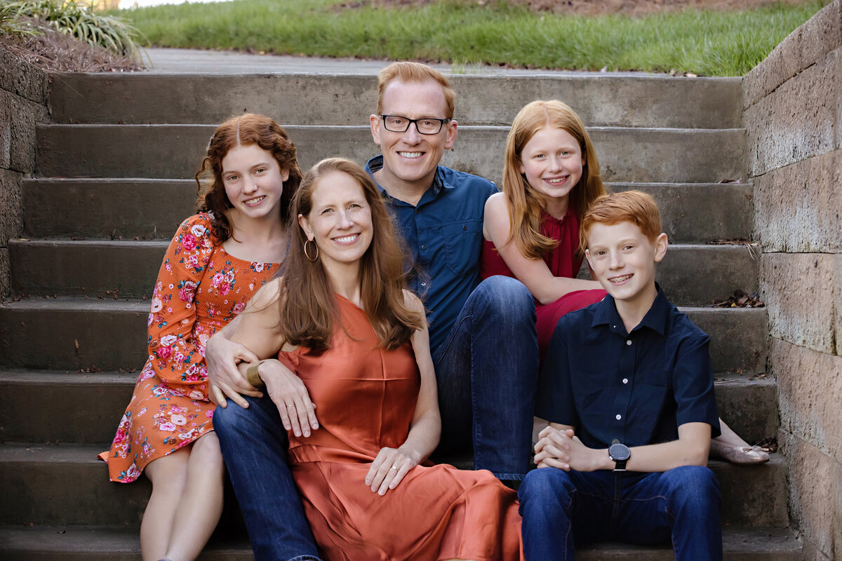 Dynamic autumn family photo of parents and three kids on weathered concrete staircase at Ballantyne Corporate Park Charlotte NC