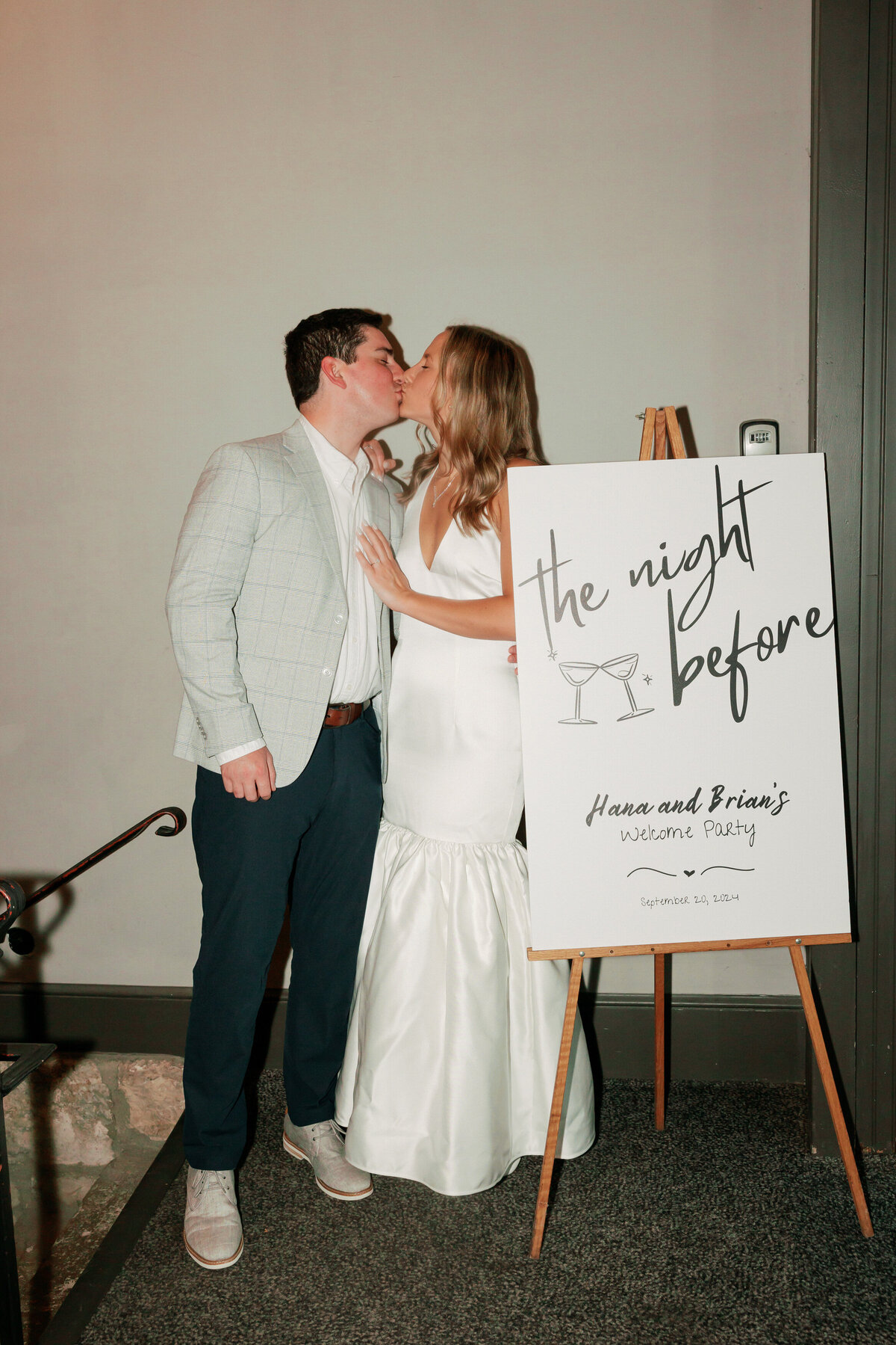 Couple kissing beside a welcome sign at their pre-wedding party, captured by a Philadelphia wedding photographer.