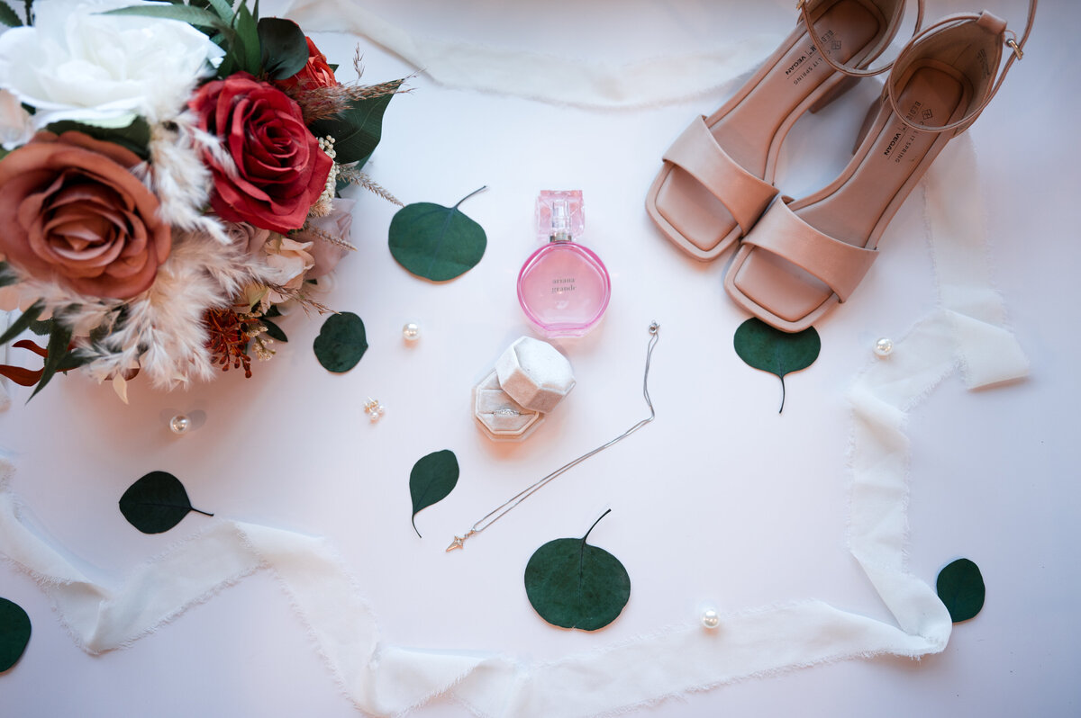 shoes, wedding rings, bridal boquet on flat lay along with mixed leaves and ribbon for a detail photo of the brides accessories