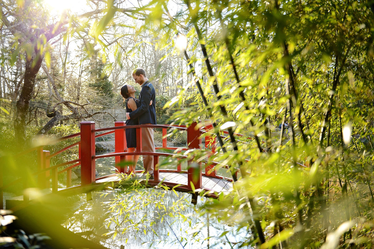 couple cuddling in Birmingham Botanical Gardens engagement session on red bridge