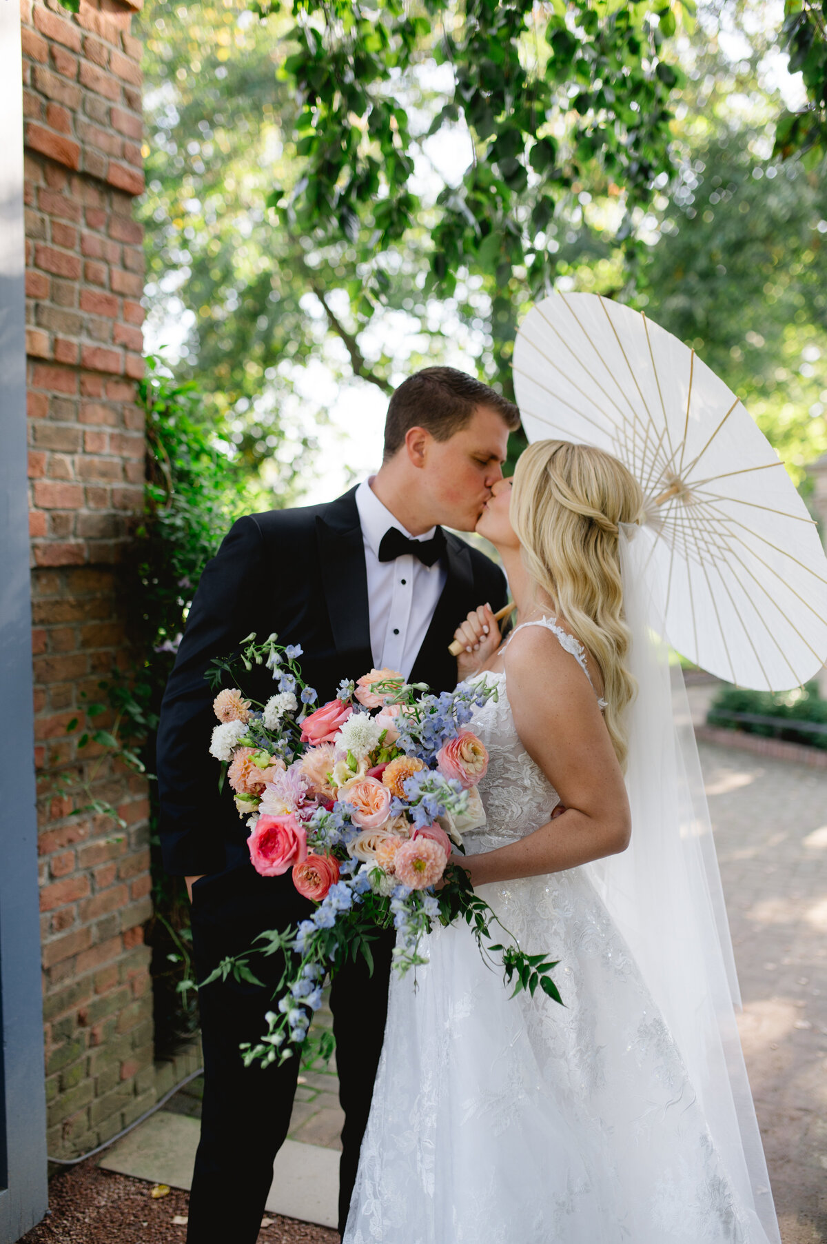 Bride and groom sharing a kiss under a white parasol in the Chicago Botanic Gardens.