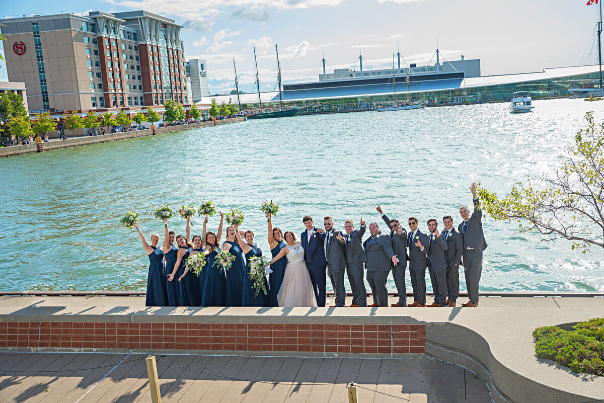 Wedding party with hands in the air by Presque Isle Bay with Erie Convention Center in background.
