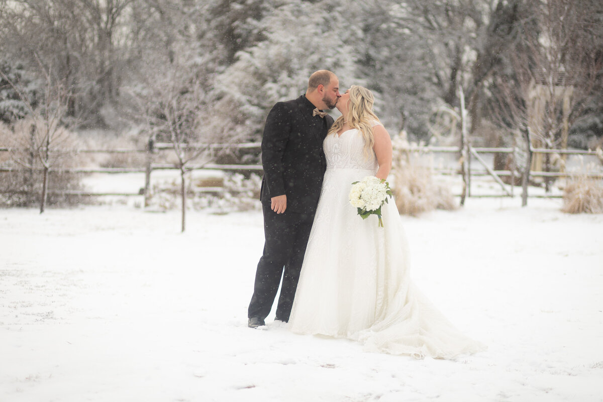 bride and groom kissing in the snow with a wooden fence in background