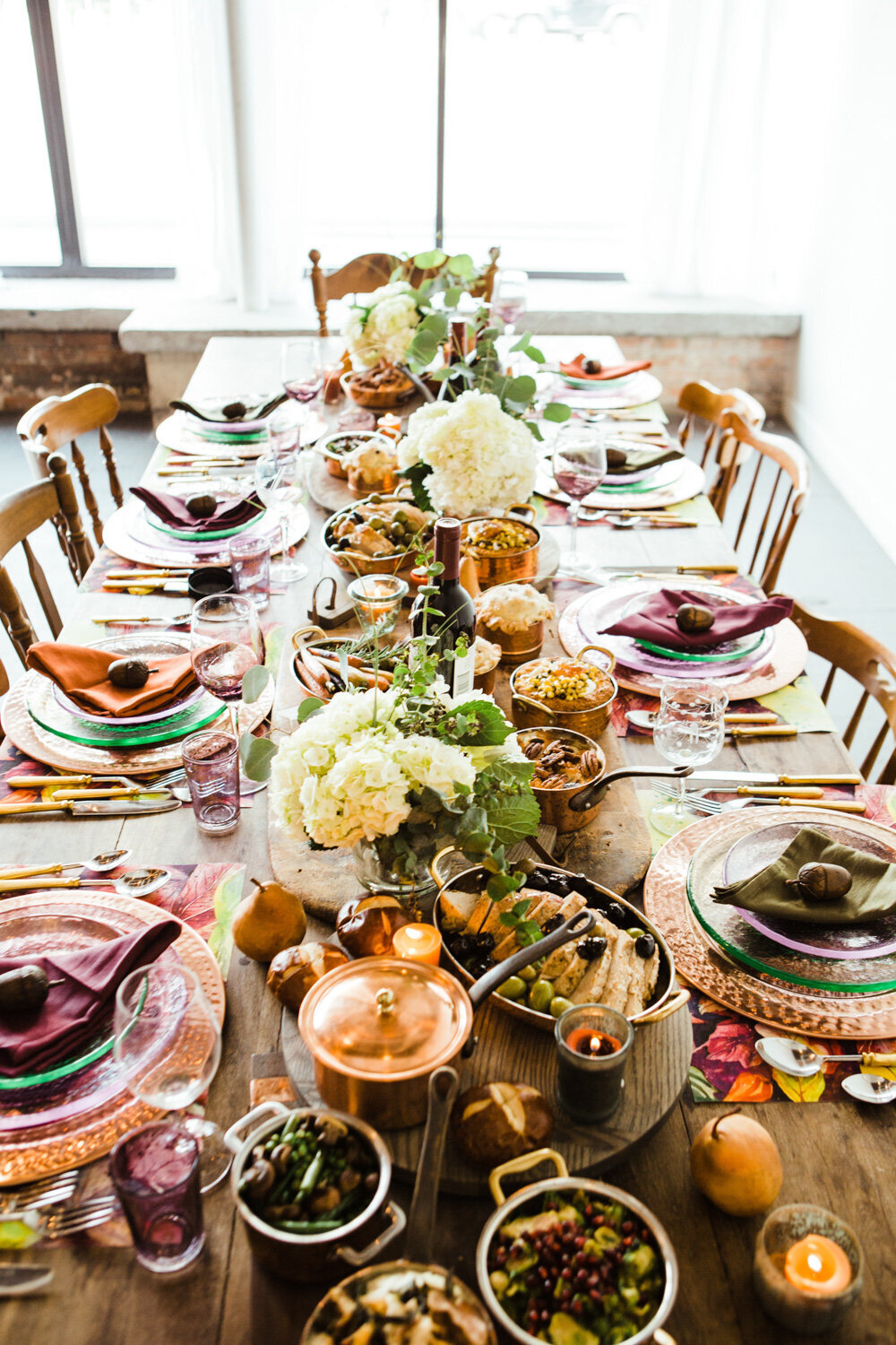 Rectangular dining table with foods, plates, utensils, glasses and centerpiece flowers
