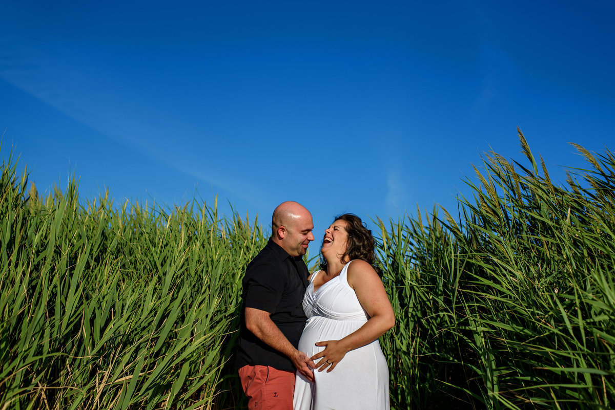 New parents laugh in the tall grass at the beach.