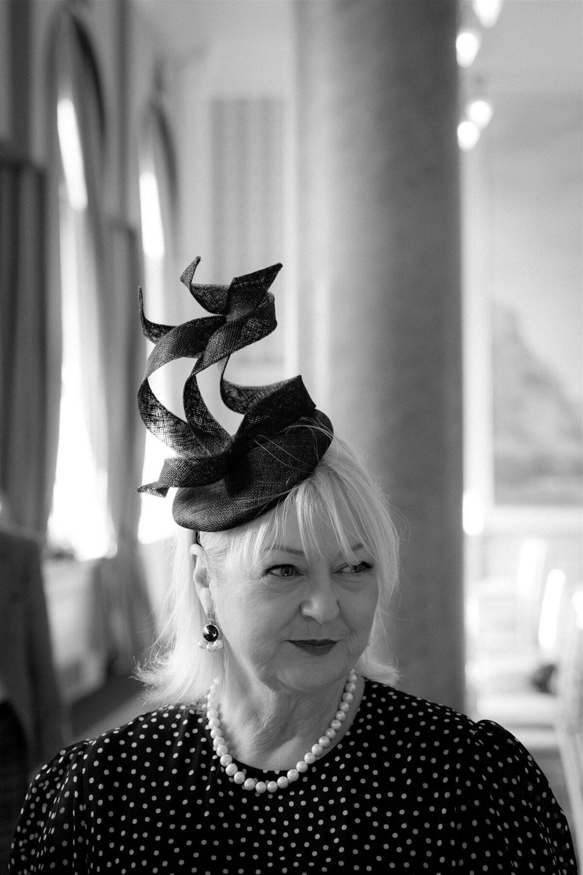 A wedding guest wears a hat that spirals upwards and twists