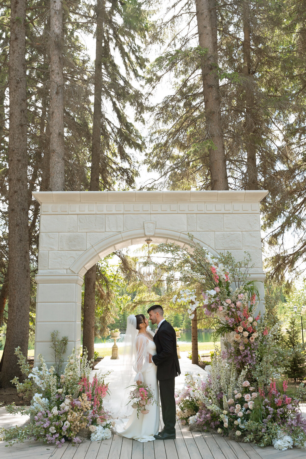 Couple standing at stunning ceremony arch at Archway Manor Weddings & Events, elegant, timeless, European-inspired Red Deer, Alberta wedding venue, featured on the Brontë Bride Vendor Guide.