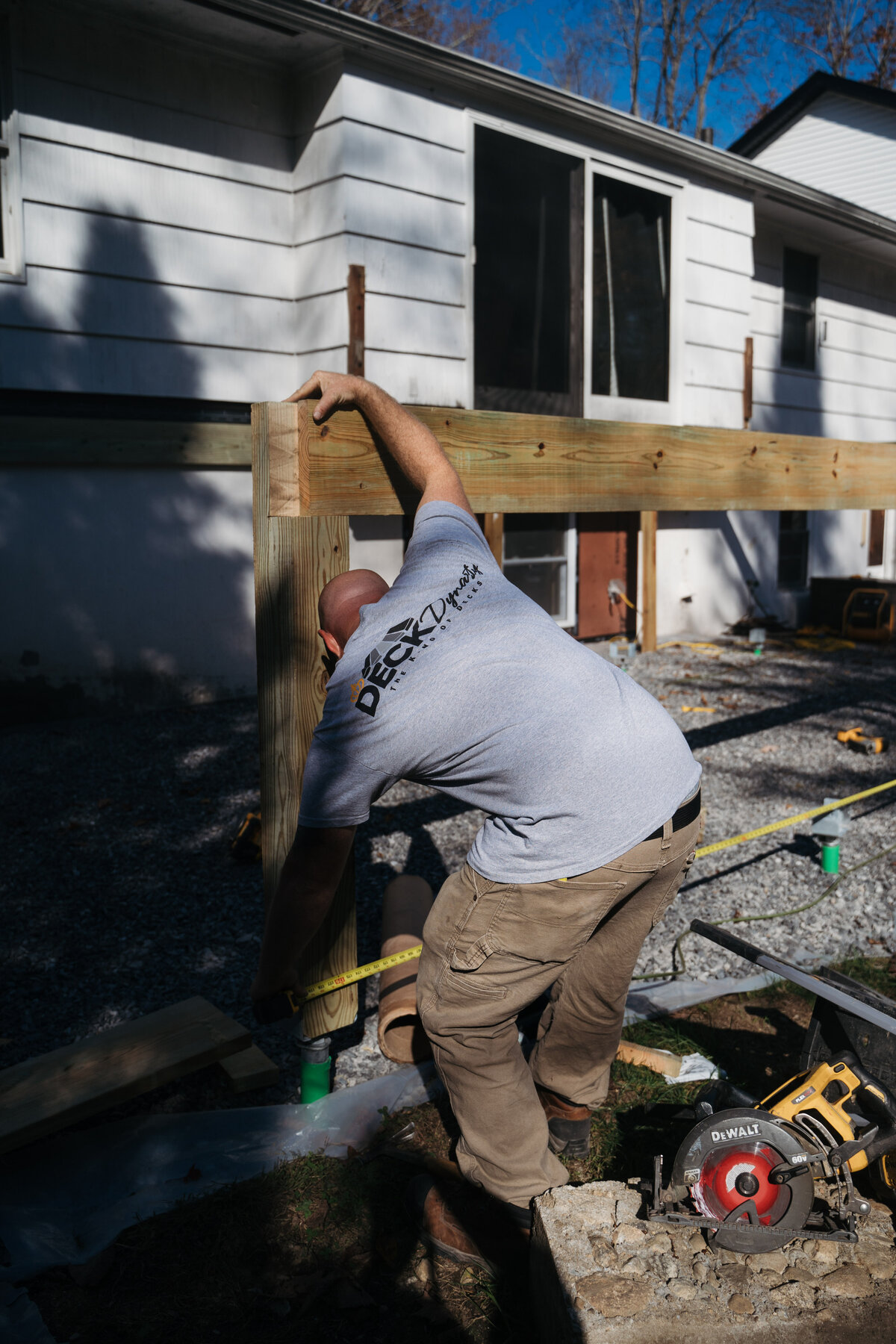 A Worcester Deck Builder works on wood framing and footing of a new build deck with measuring tape