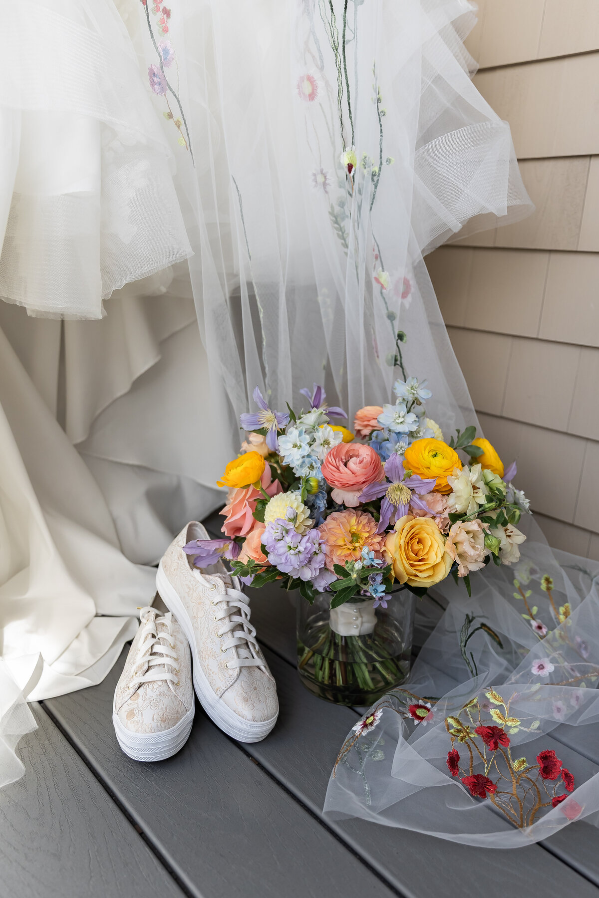 Wedding Photographers in RI | Kelsey Sheehan Photography Timeless Rhode Island Weddings | A colorful bridal bouquet with pastel flowers, white sneakers, and a sheer embroidered veil set against a softly lit background, conveying a casual elegance.
