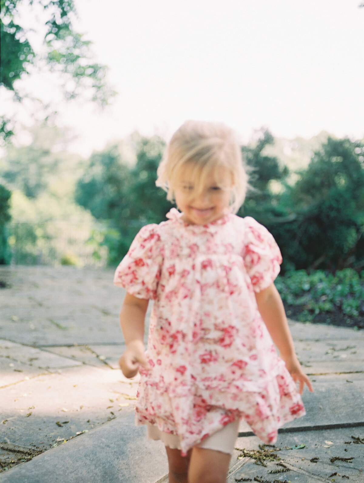 Blonde little girl walks along a stone walkway, slightly out-of-focus.