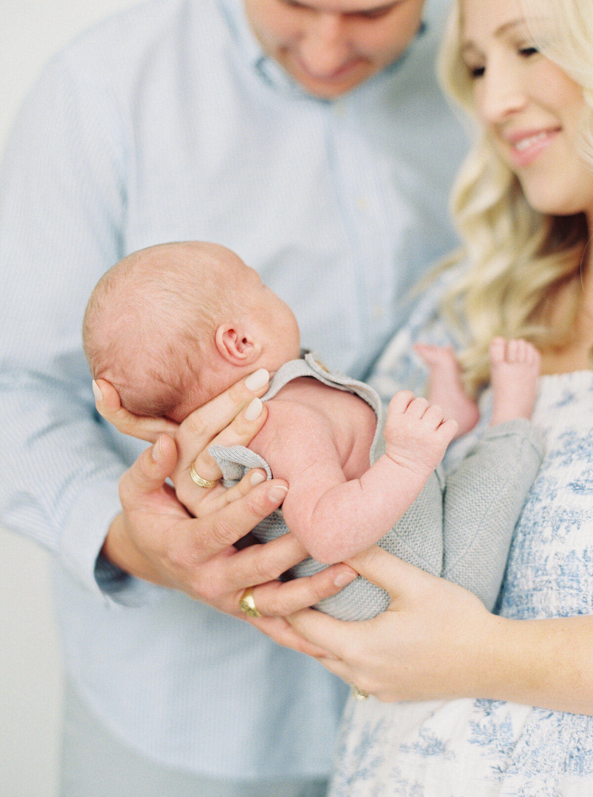 New parents hold their son and look lovingly at him. Image by Raleigh newborn photographer A.J. Dunlap Photography.