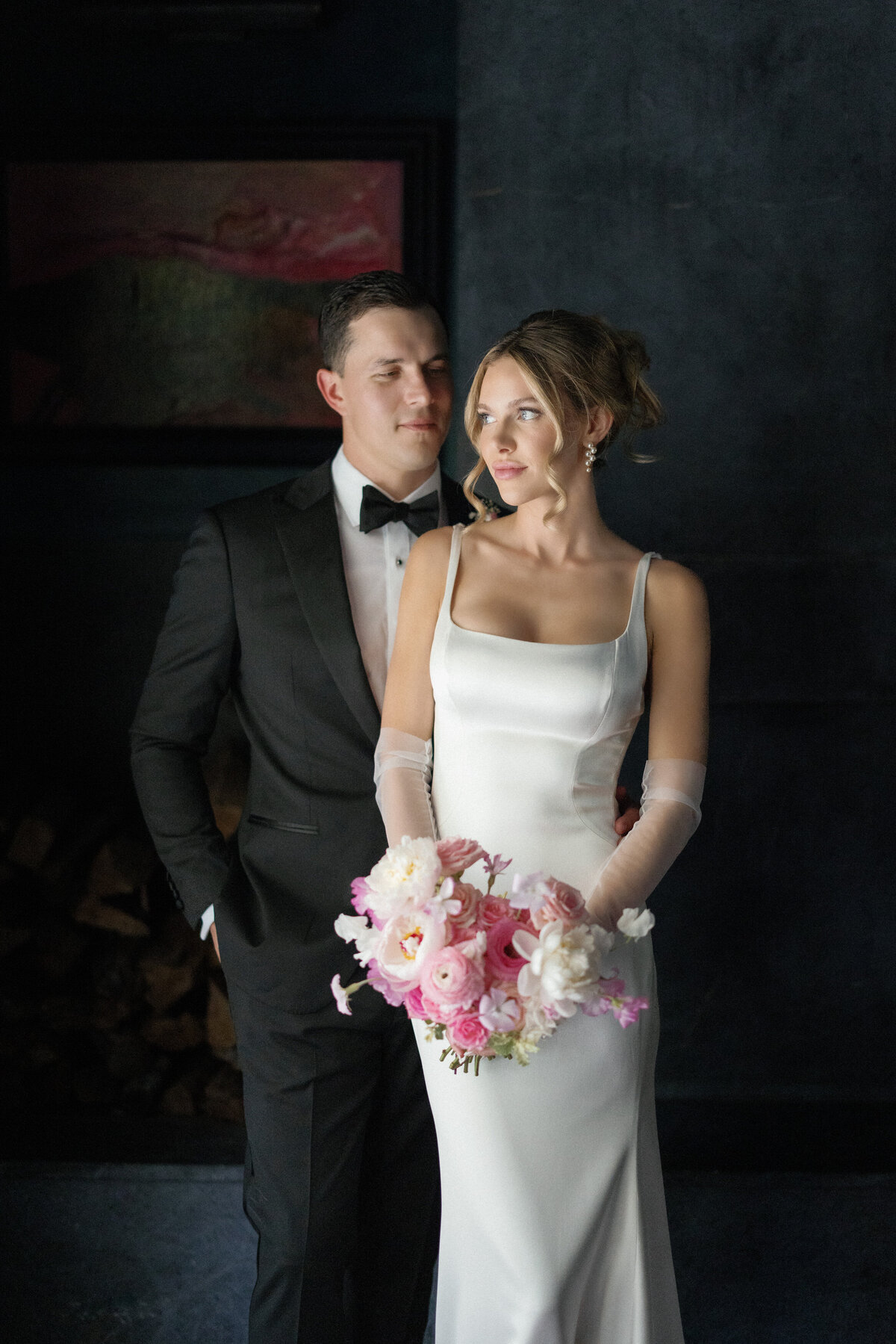 groom and bride holding pink bouquet in dark room