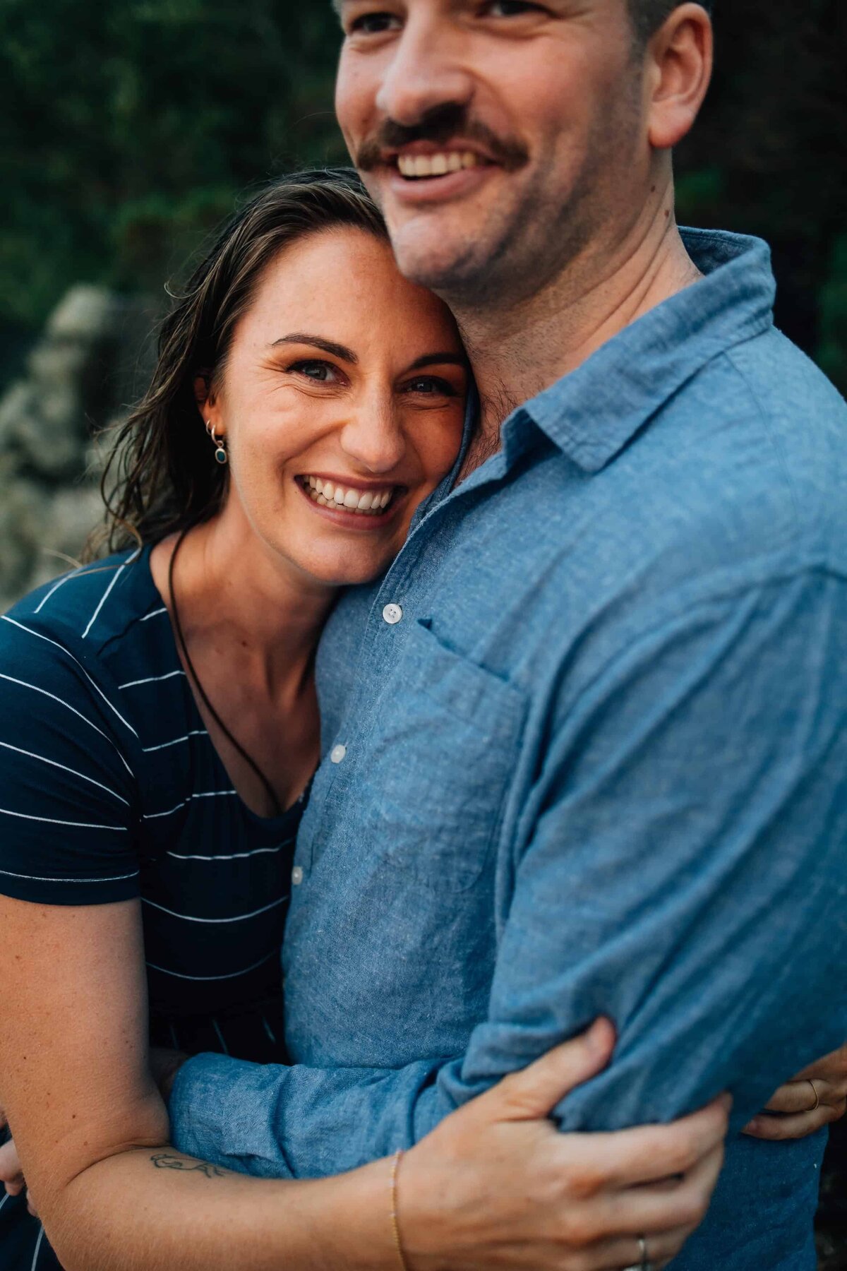 Woman with head on mans chest, smiling at camera during maternity photoshoot Melbourne.
