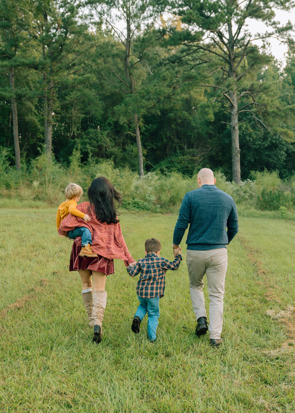 Family of 4 walking away from the camera in a grassy field