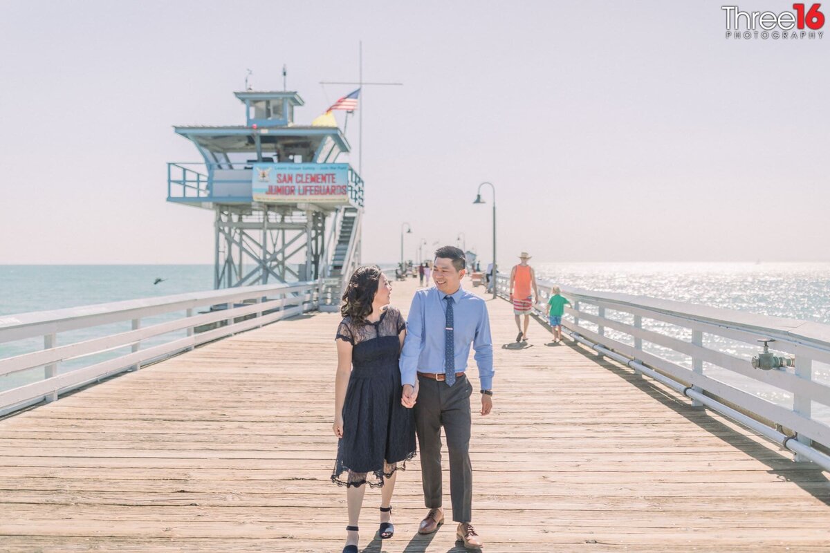 Engaged couple walk along the San Clemente Pier holding hands