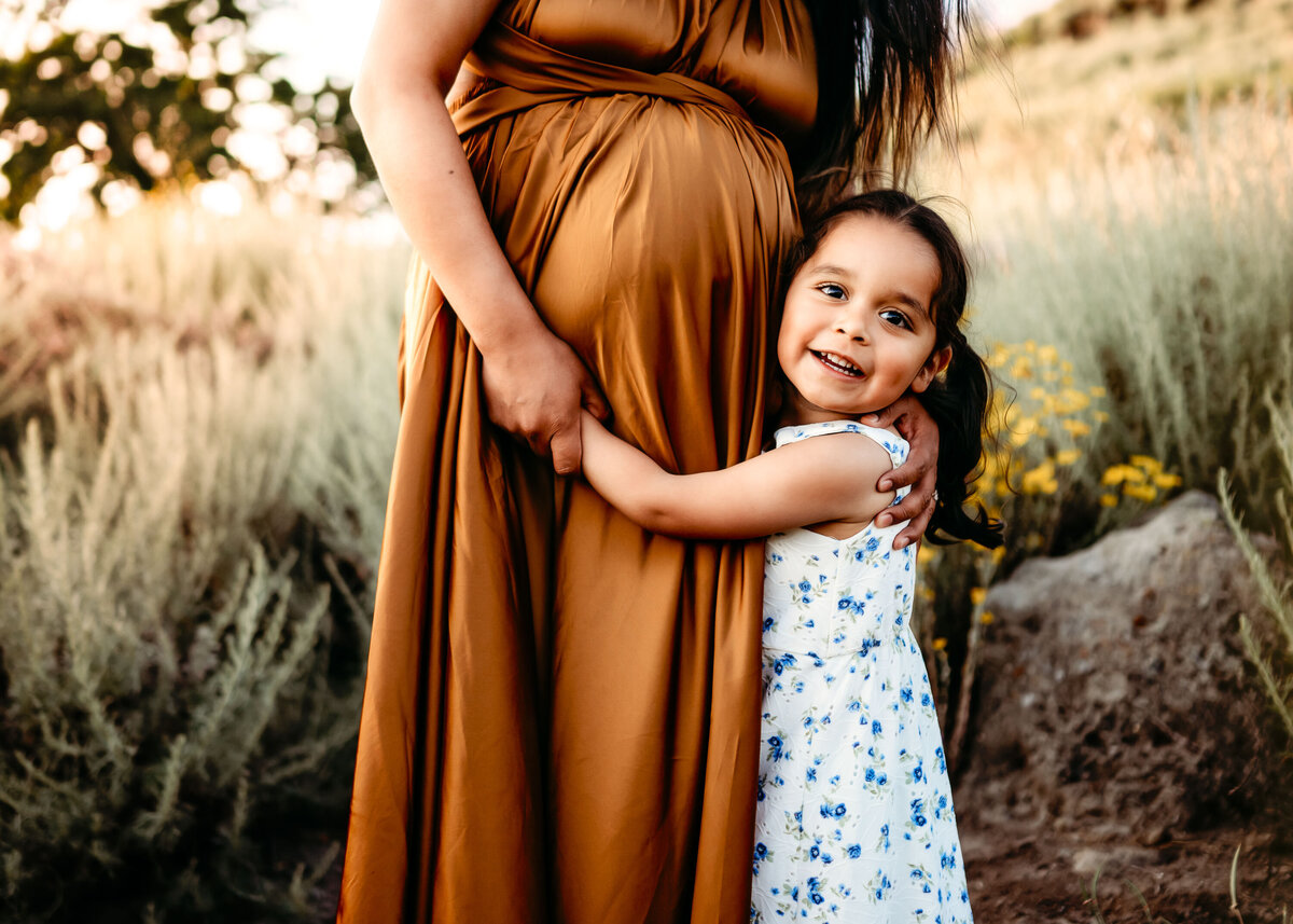 Toddler hugs pregnant moms belly - her maternity dress is gold.