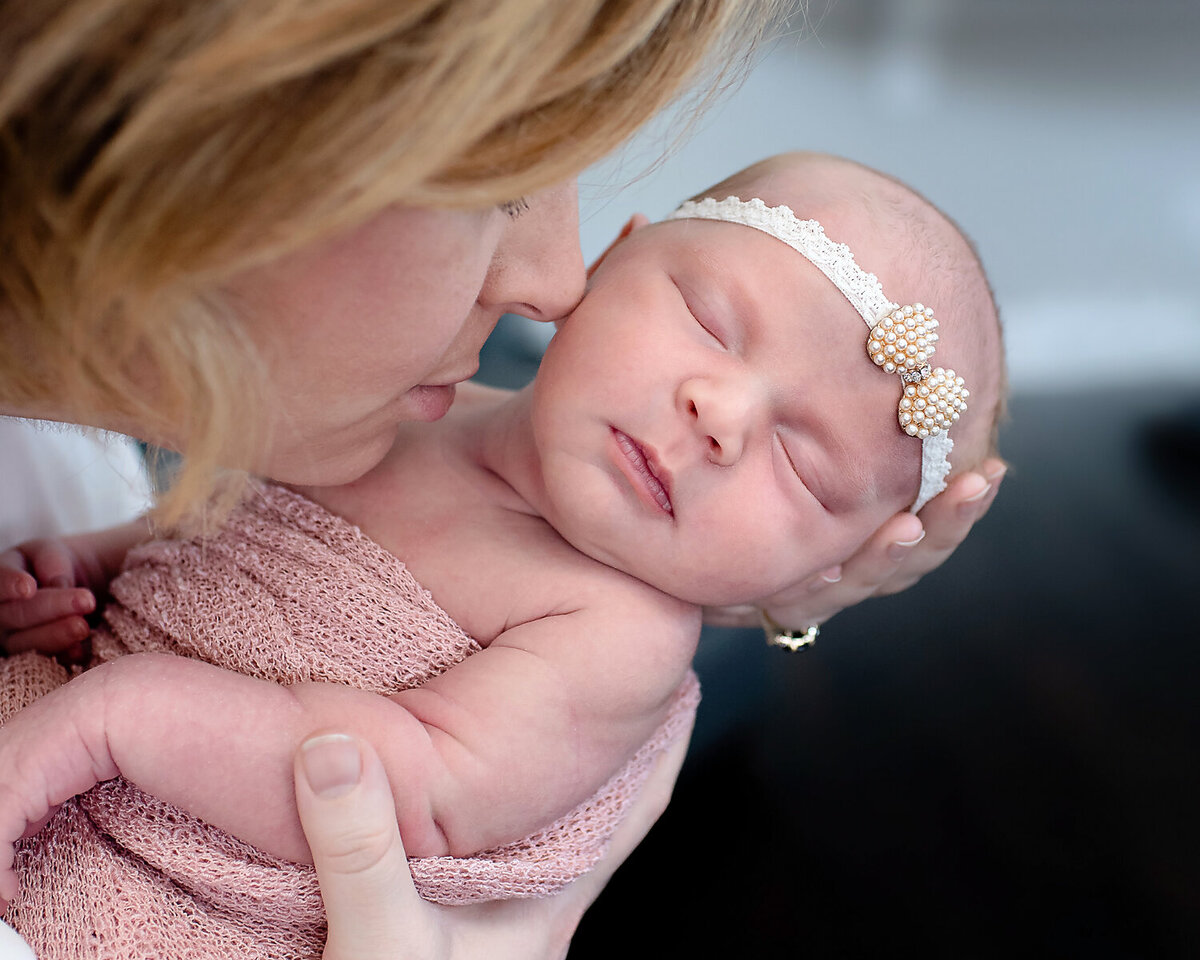 A new mom resting her nose on her newborn baby daughter's cheek while she sleeps in her arms.