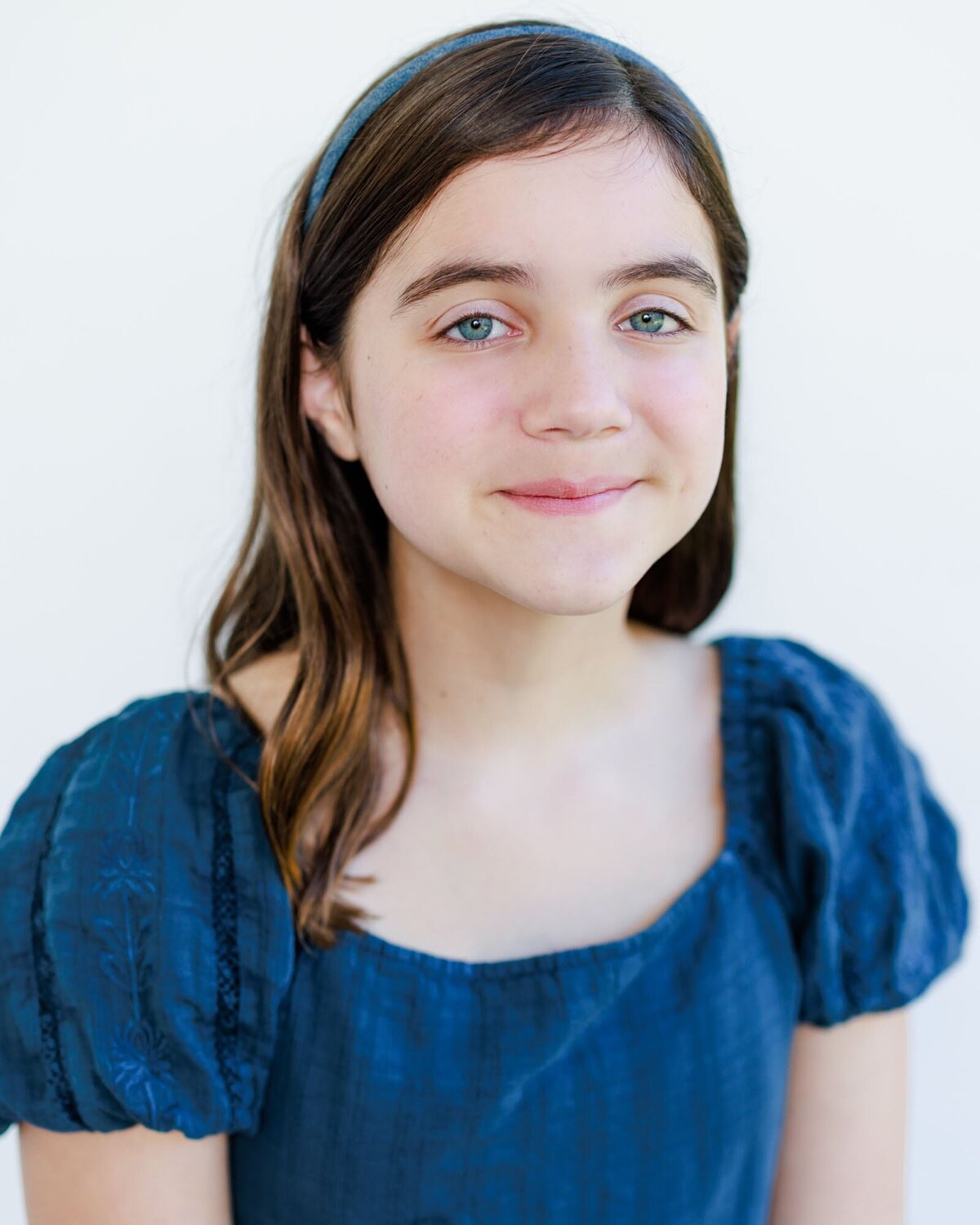 Headshot of a girl actor wearing a blue dress on a white background.