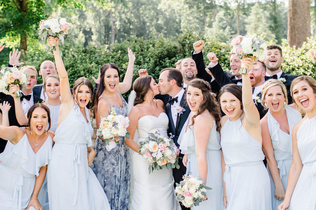 bride and groom kissing while surrounded by bridal party